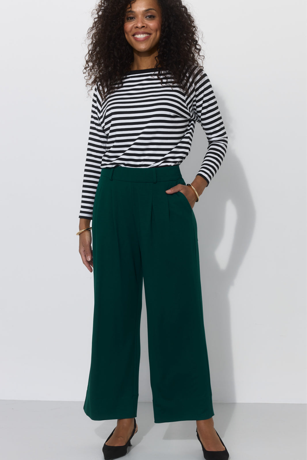 Kobieta w zielonych spodniach typu culottes i koszulce w paski, stylowy strój na co dzień