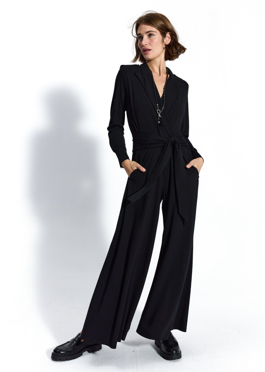 Czarny jumpsuit z wiązaniem w pasie, idealny na co dzień lub na imprezę, z kieszeniami i eleganckimi butami.