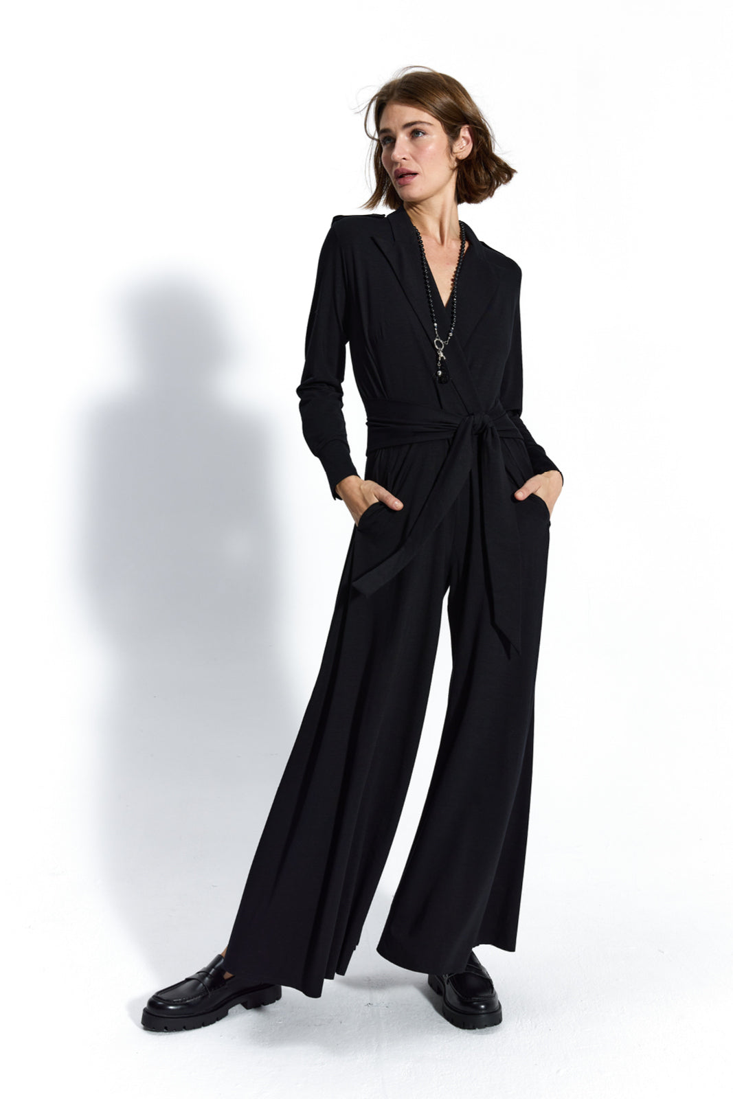 Czarny jumpsuit z wiązaniem w pasie, idealny na co dzień lub na imprezę, z kieszeniami i eleganckimi butami.